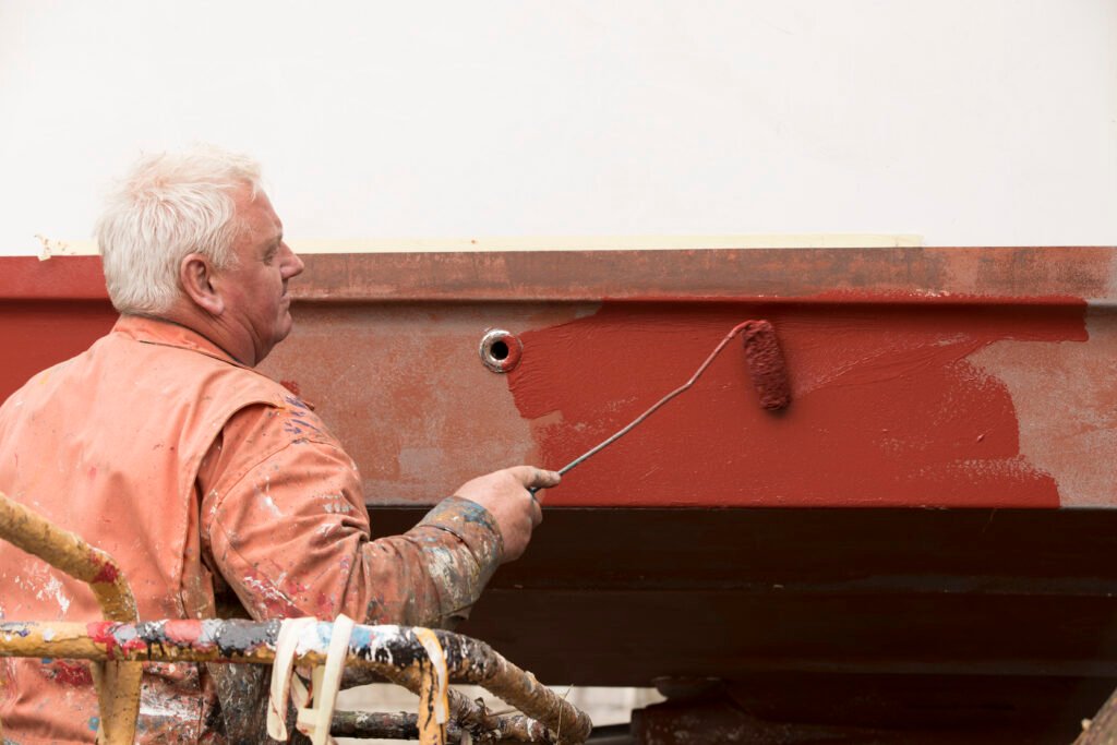 Senior male ship painter roller painting ship hull red in ship painters yard Divi landing stress management